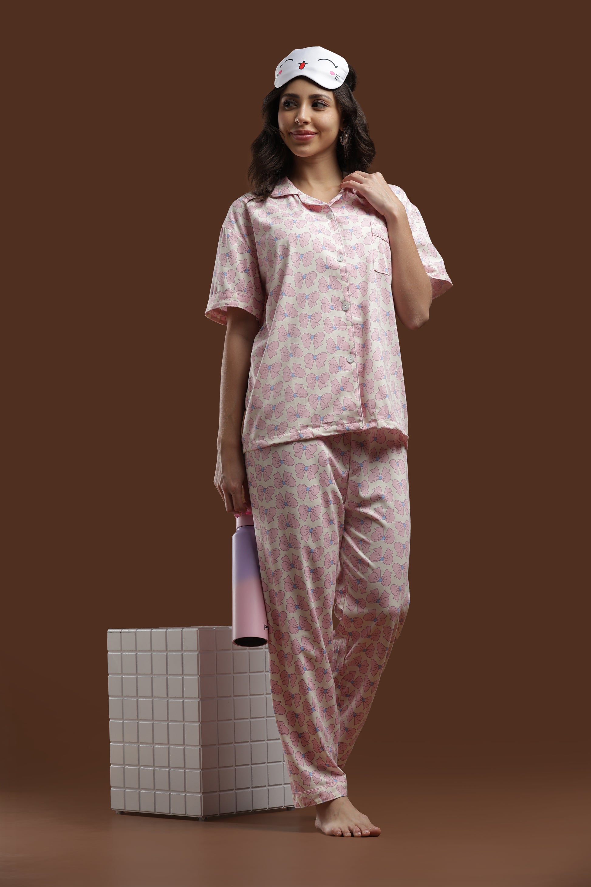 A full-length view of the Koozy pink ribbon PJ set for women, styled against a warm brown backdrop. This Pinterest-inspired, breathable cotton set is designed for a beautifully printed, soft morning look.