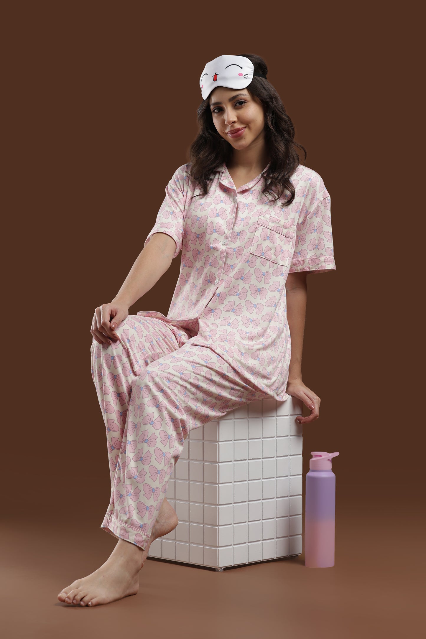 close-up of a woman in the koozy pink ribbon print nightwear suite, styled with a cute bunny sleep mask on her head. highlights the soft, breathable fabric of the short-sleeve top and matching pants.