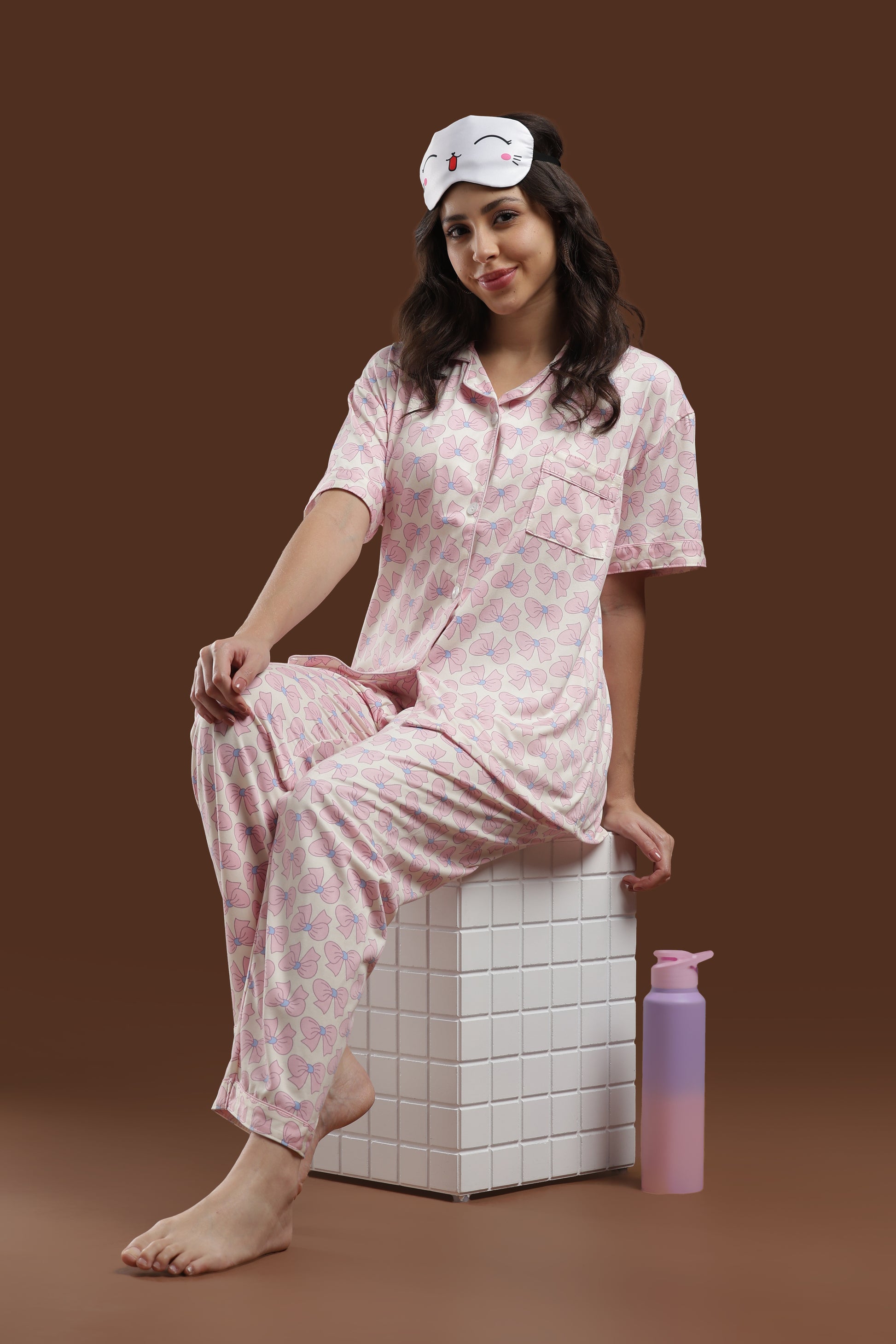 Close-up of a woman in the Koozy pink ribbon print nightwear suite, styled with a cute bunny sleep mask on her head. Highlights the soft, breathable fabric of the short-sleeve top and matching pants.