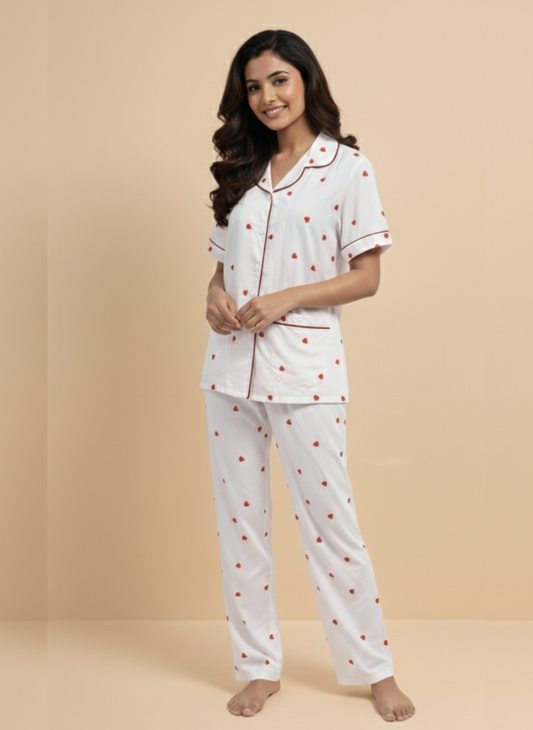 Effortlessly cute and comfortable Koozy Sweetheart pajama set in white with red heart prints. A Pinterest-style collared nightwear suite made from breathable cotton fabric, featuring a short-sleeve button-down top with red contrast piping and matching long pants. Relaxed fit, beautifully printed PJ set for a soft, easy, and cozy look.